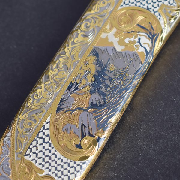 The scabbard of the knife is covered with gold and a carved pattern. In the front part is a picture of mountains and forests. Give a bright accent to sheath artistic enameling
