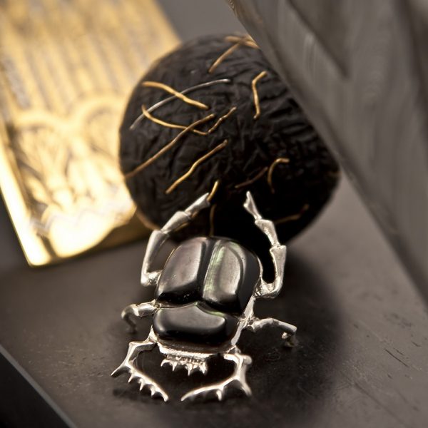 According to the beliefs of the ancient Egyptians, a scarab rolls its ball with the seeds of life from east to west, like the sun passes through the sky. On the slope of the mountain where the scarab rolls a ball, the “Ankh” sign is depicted – a key of life and a symbol of immortality, b