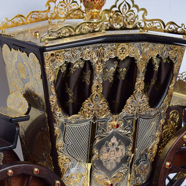 A large wooden carriage decorated with decorative slips. The surface of the linings is decorated with relief engraving and gilding.