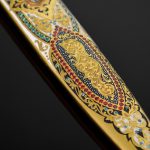 The scabbard is decorated with an ornament with the addition of enamel and gold, as well as cubic zirconias of different colors.